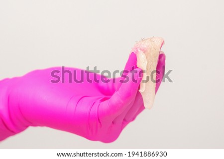 Close up of the hand of a beautician in pink glove holding white sugar paste with removed hair against a white background