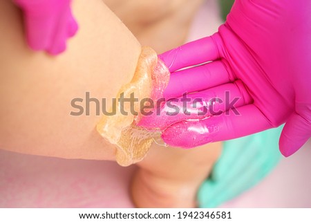 Two female cosmetologists waxing woman\'s legs with hot sugar paste in a beauty spa salon