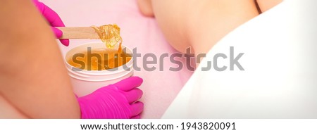 Cosmetologists waxing female legs with hot sugar paste in a beauty spa salon
