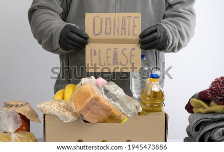 man holds a sheet of paper with a lettering  donate please and collects food, fruits and things in a cardboard box to help the needy and the poor, the concept of help and volunteering