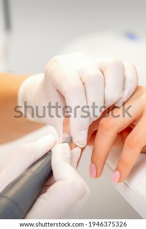Manicure master applying electric nail file machine removing old nail polish on fingernails in a nail salon