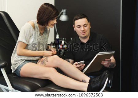 Man and woman choosing tattoo design in studio. Professional male tattooist discussing sketch with young client, copy space
