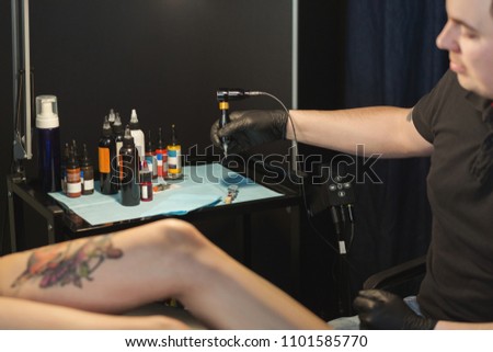 Professional tattoo artist making beautiful tattoo on young woman leg. Man tattooist drawing picture on female body with special machine, copy space