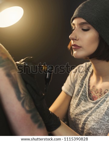 Concentrated woman tattooist doing tattoo with tattoo machine on male shoulder. Unusual female profession, copy space