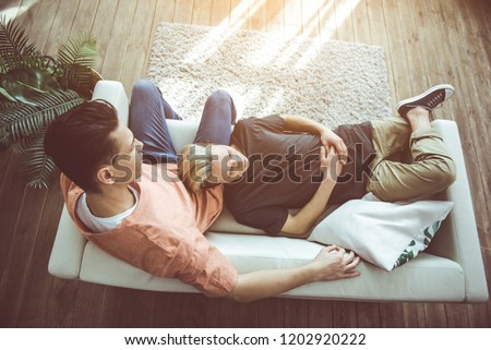 Top view portrait of guy with dyed hair lying on sofa while his boyfriend sitting and looking at him