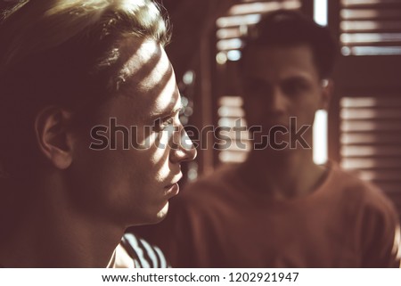 Close up toned portrait of attractive guy with shadow from jalousie on his face looking away with serious expression. Dark-haired man on blurred background