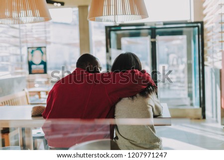 Caring young man wearing warm jacket and kindly putting his hand on the shoulder of his beloved woman while sitting in the cafe with her