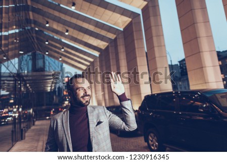 Attractive young man feeling good and smiling while walking near the building and waving his hand