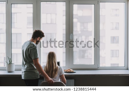 Back view of woman sitting at table with laptop and her boyfriend standing next to her. Copy space on right side