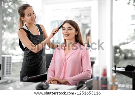 Waist up of smiling lady looking in the mirror while female stylist combing her hair