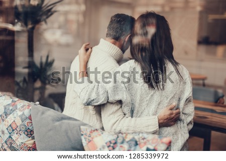 Beautiful couple sitting in small cafe with bright interior. They hugging each other and relaxing