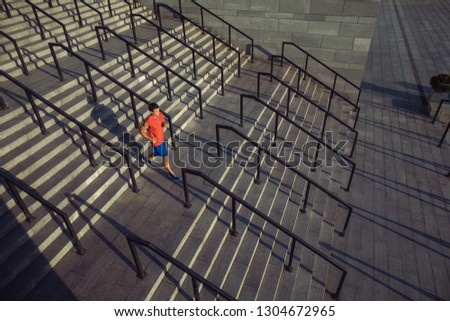 Full length side view orderly man listening audio with headsets while running on stairs outdoor