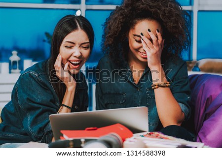 Oh my god, what is picture. Laughing asian and african female having fun while looking at screen of computer