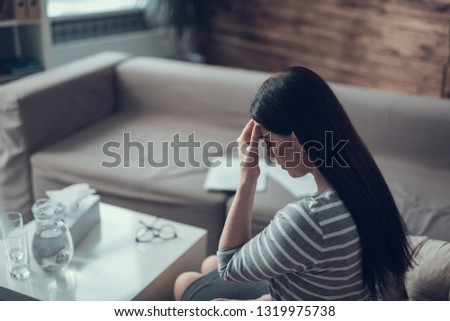Young sad lady sitting alone at table in living-room while feeling headache. Stress concept
