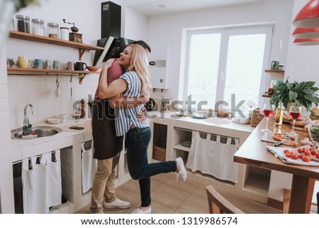 Full length portrait of man in apron embracing his charming wife while she smiling