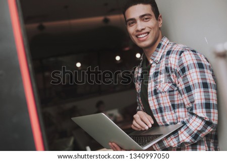 Waist up portrait of handsome guy with silver notebook looking at camera and smiling