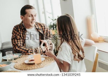 Calm man sitting at the table and looking at his daughter while talking to her during the breakfast