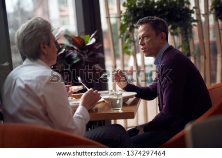 Enjoyable meetings. Waist up side on portrait of mature male and female having dinner in cafe and discussing something
