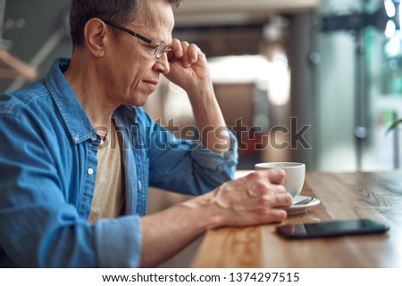 Technology in our life. Close up side on portrait of smiling aged male in glasses sitting with cup of coffee in cafe alone
