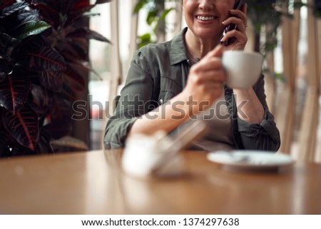 Close up cropped head portrait of smiling stylish aged lady talking on mobile phone sitting in cafe with cup of coffee