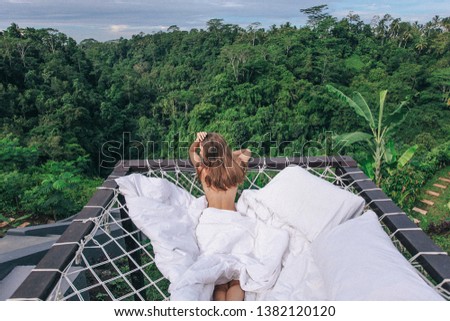 travel series. photo of beautiful woman with dark hair relaxing in open air  bed with Bali jungle view