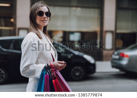 Waist up portrait of attractive elegant lady in sunglasses holding colorful shopping bags and smiling. Copy space in right side