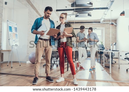 Full length portrait of joyful colleagues staying in meeting room and looking on folder with project with partners on background