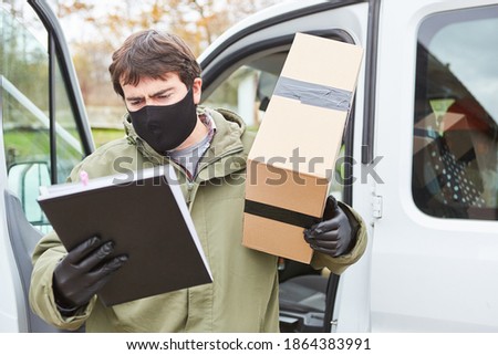 Parcel delivery man with face mask because of Covid-19 with package looks at delivery note for delivery at Christmas