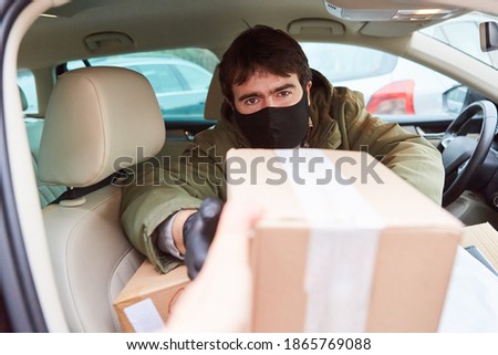 Parcel delivery man in the car delivers the parcel with a face mask due to Covid-19