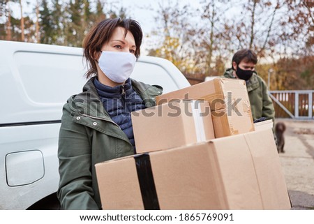 Woman with face mask because of Covid-19 as a parcel carrier with parcels as delivery for Christmas