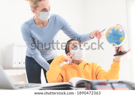Child home studying education, homeschooling, with private tutor mother with protective mask in the time of viruses, flu and seasonal pandemic.