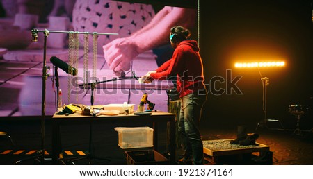 View of male sound designer in headphones recording scratching noise against screen with video of potter creating earthenware in workshop