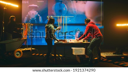 People recording various sounds against screen with 3D cartoon about robot during work in dark studio