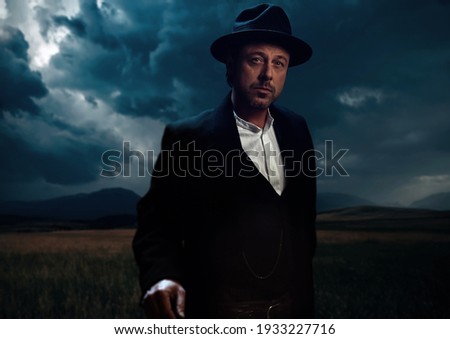 Man in victorian cowboy clothing standing on prairie area.