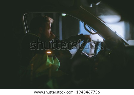 The man is alone driving a car at night. Young serious focused guy is driving in a car driving late at night in the dark