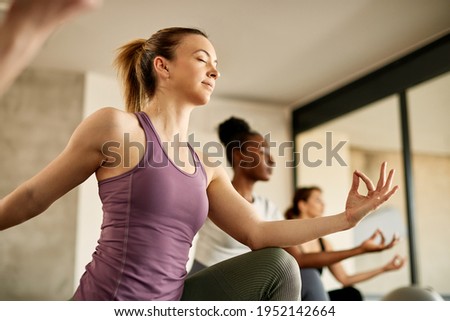 Low angle view of female athlete with eyes closed doing Yoga relaxation exercise in a health club.