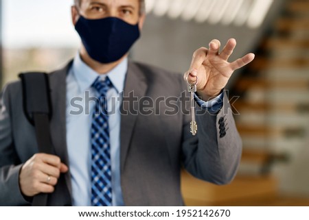 Close-up of businessman with face mask holding key of his new real estate.