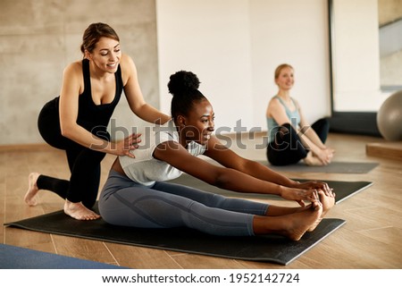 Happy African American athletic woman stretching her body while female instructor is assisting her.
