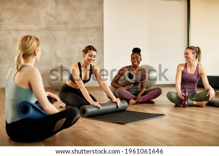 Happy athletic woman rolling up her exercise mat and having fun with her friends after sports training in health club.