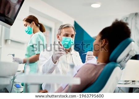 Smiling dentist communicating with African American woman while checking her teeth during dental procedure at dentist\'s office.