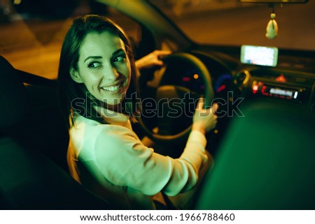Young happy woman drives car in a reverse at night.