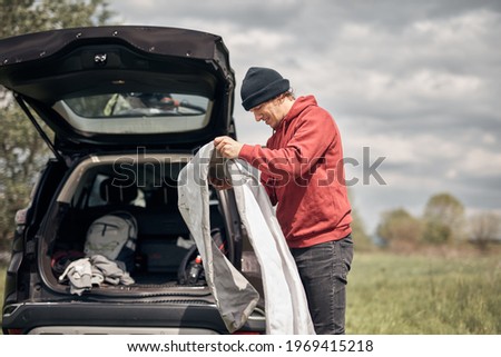 Camper packing and unpacking from a car\'s roof rack in nature.