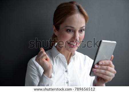 Portrait of happy businesswoman watching at phone while keeping it in arm. Technology and job concept