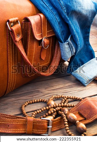 orange leather vintage suitcase travel bag, old fashioned beads and jeans on a wooden floor