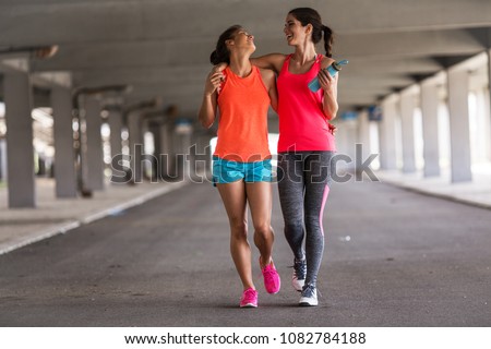 Couple of female friends jogging on the city street under the city road overpass.They relaxing after jogging and making fun.Embracing each other.