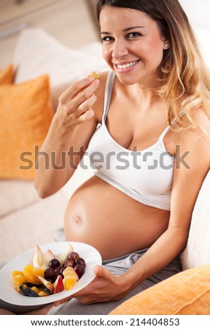 Pregnant woman sitting in her living room and eating fruits