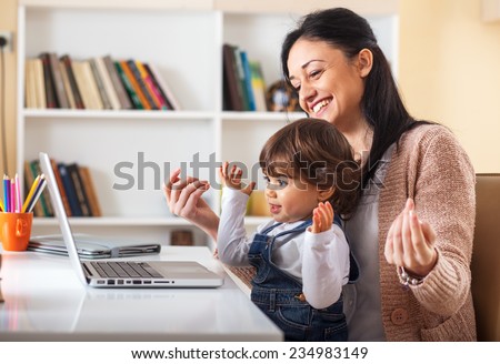 Mother and her baby girl listening to music on laptop.They sitting in living room.Natural light ambient.