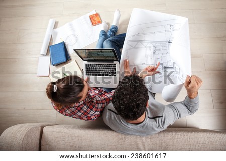 Young couple sitting on the floor and looking at the blueprint of new home.Investment.