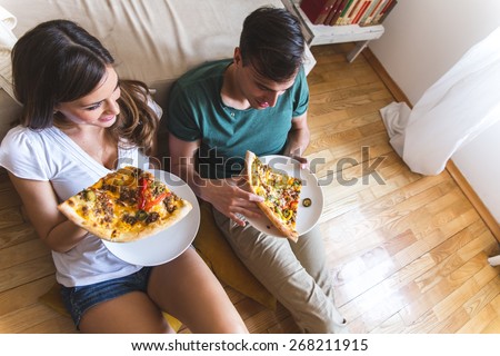 Young couple eating pizza.They sitting on floor and joying in hot pizza.Image taken from above.
