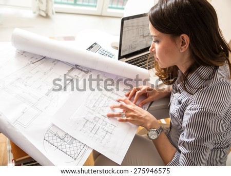 Female architect working at home.She looking blueprints.